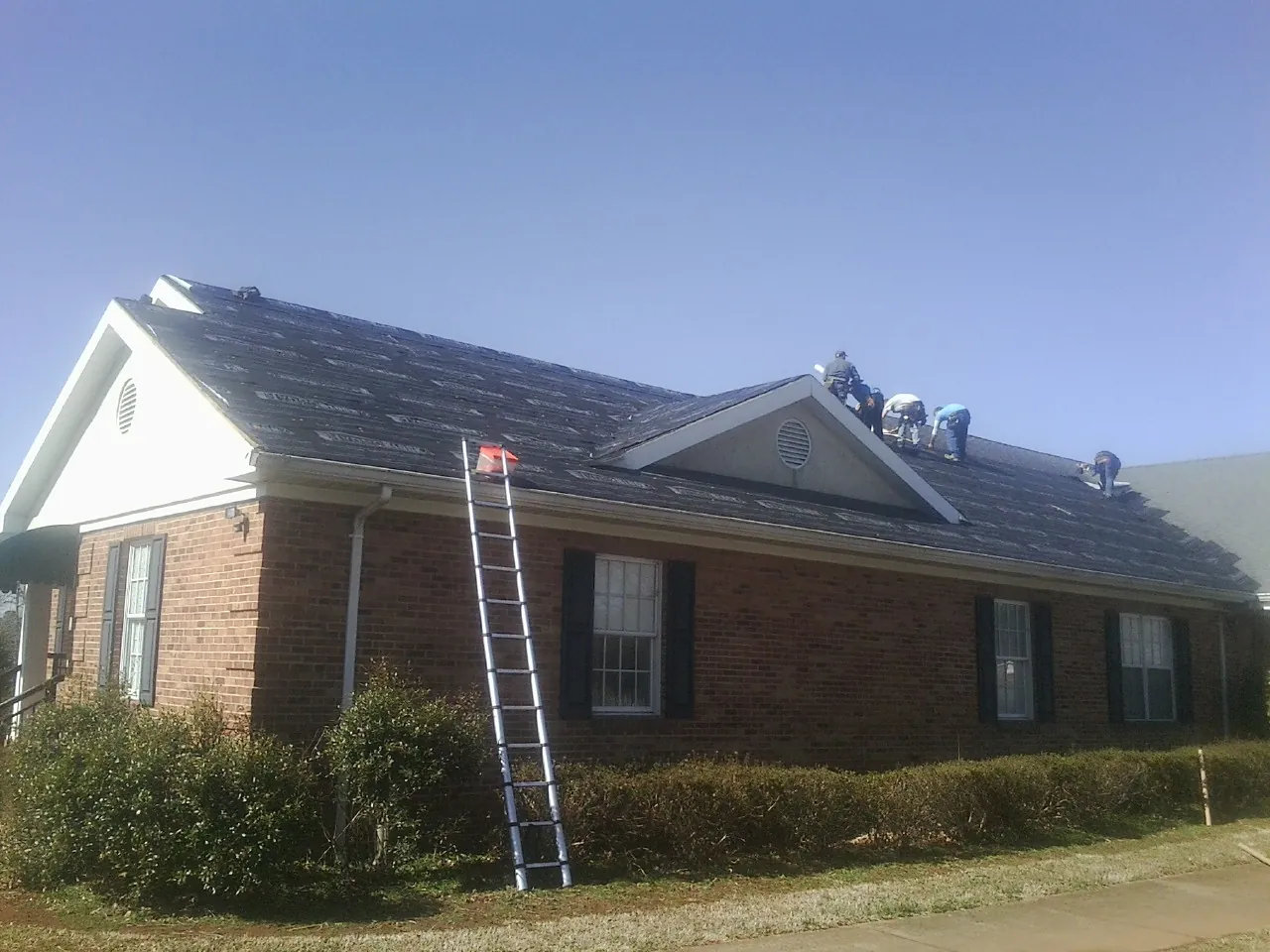 Crew tearing shingles off a brick ranch roof with a ladder set — Emergency Roof Repair work by our crew in Daufuskie Island