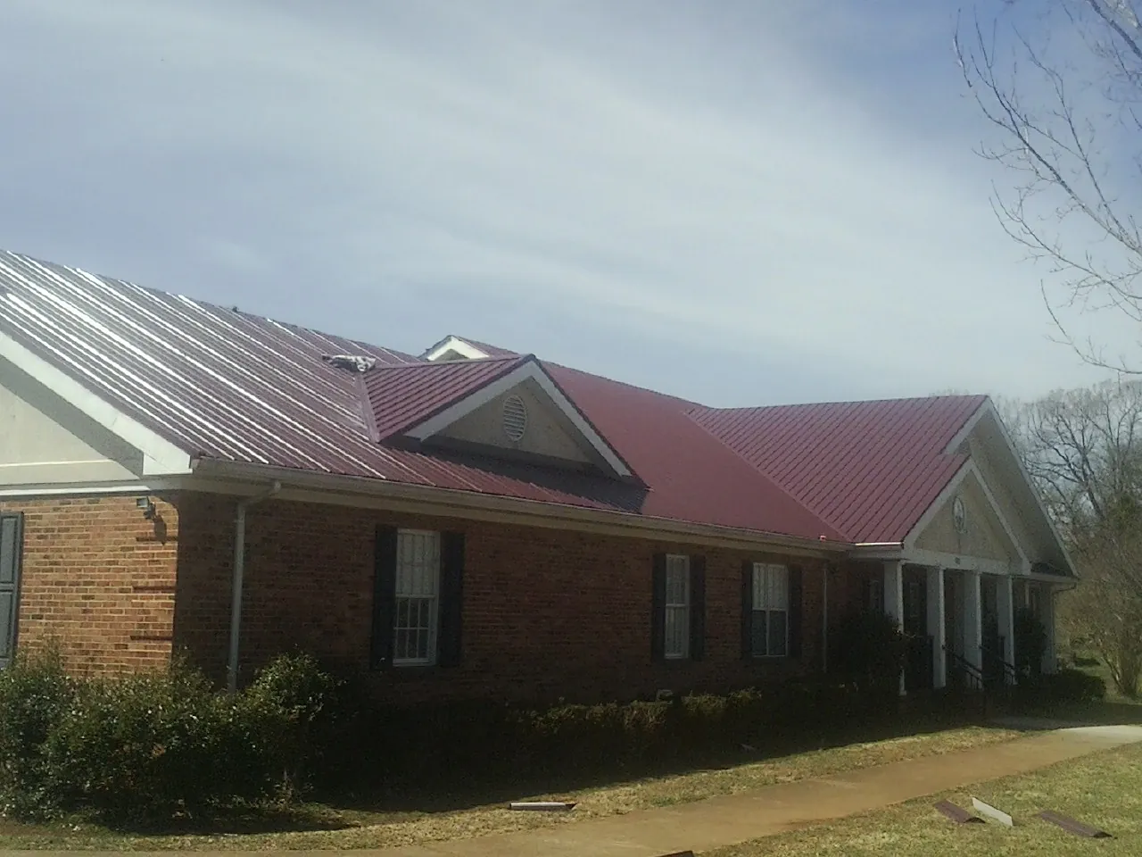 Red metal roof with gabled entries on a long brick building, from a Hail Damage Roof Repair job in Daufuskie Island