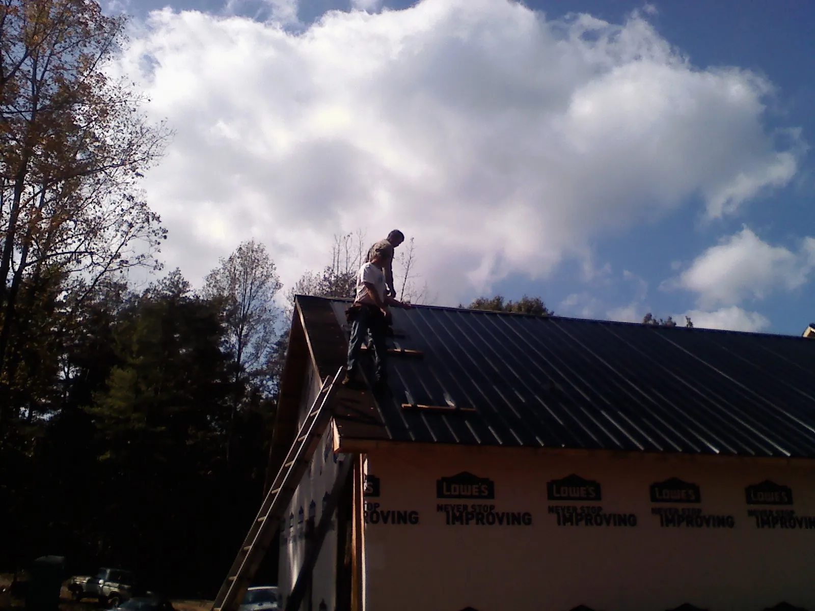 Roofer fastening dark metal panels high against a cloudy sky, from a Roof Inspection job in Daufuskie Island