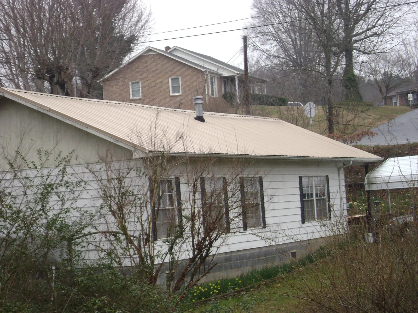 Tan metal roof on a white sided house set into a hillside — Commercial Roofing by Roofing Brothers in Daufuskie Island